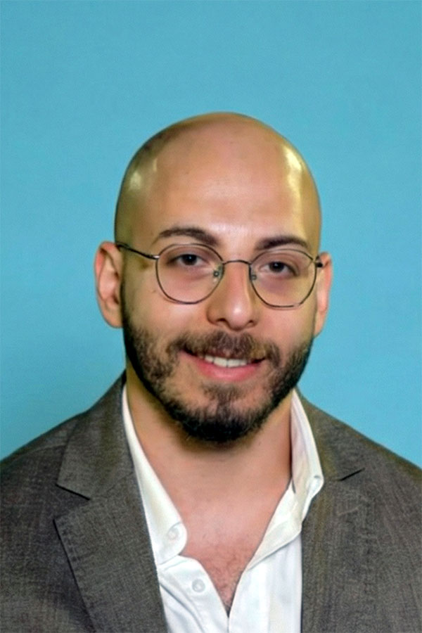 Scientist specializing in epigenome regulation and cancer vaccine development, wearing a gray blazer and white shirt, posed against a plain blue background.